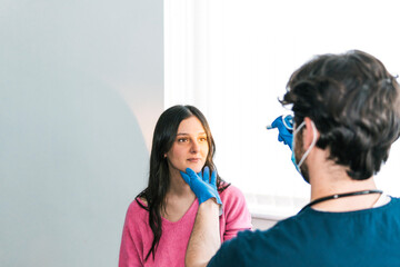 A medical professional in gloves palpates the neck of a patient, checking for swollen lymph nodes in a routine exam
