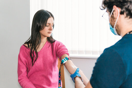 A young patient anxiously looks away as a medical technician prepares to collect a blood sample for laboratory testing