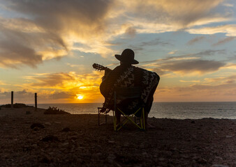 Musician Composing while playing the guitar by the Sea at Sunset