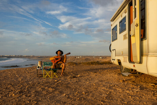 Nomadic musician composing by the sea at sunset - Powered by Adobe