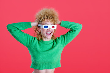 A woman with bouncy curly hair is all smiles in 3D glasses, sporting a lively green sweater against a captivating red background