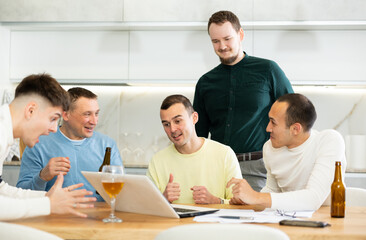 Obraz premium Group of male friends gathering at home enthusiastically celebrating good news, seen on laptop screen, with lively gestures and drinks..