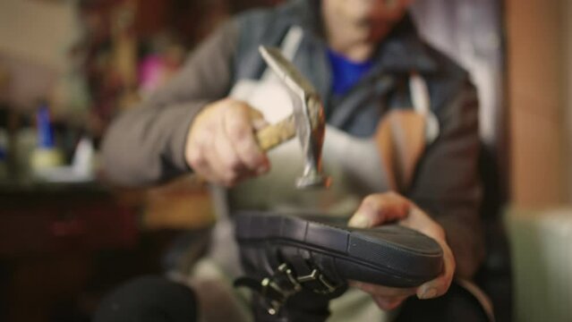 Close up senior cobbler hitting with hammer shoe sole and repairing shoe.
