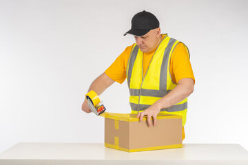 Man packer at work. Warehouse worker seals box with tape. Dispenser with tape in hands man. Packer...