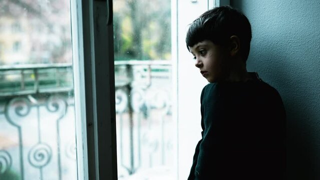 One young boy struggles with mental illness at home with green tint color. Child depressed standing by window with blank expression depicting a meaningless life