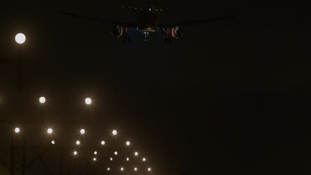 Airplane is shown in alignment for landing, with its bright landing lights and underwing illumination, against a backdrop of runway lights under a night sky