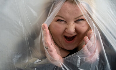 mischievously maliciously laughing woman sticks her head and hands out of the plastic foil wrap,...