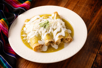 Green enchiladas. Typical Mexican dish made with a folded or rolled corn tortilla filled with shredded chicken and covered with spicy green sauce, cream, grated cheese and onion. - 775442277