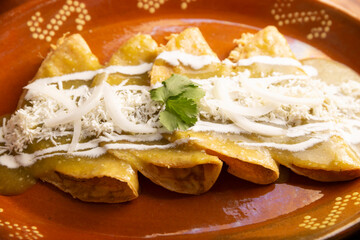 Green enchiladas. Typical Mexican dish made with a folded or rolled corn tortilla filled with shredded chicken and covered with spicy green sauce, cream, grated cheese and onion. - 775442451