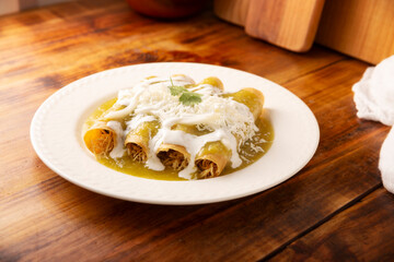 Green enchiladas. Typical Mexican dish made with a folded or rolled corn tortilla filled with shredded chicken and covered with spicy green sauce, cream, grated cheese and onion. - 775442876