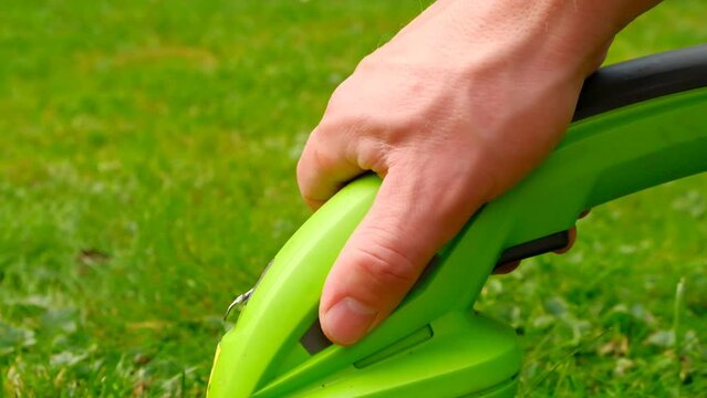 electric trimmer in a mans hand close-up cuts the grass.lawn trimmer.The process of cutting grass close-up.Garden equipment and tools. 4k footage