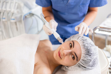 Positive young woman getting hardware facial procedure using ion bubble pen of hydrogen oxygen...
