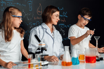 Teacher in support and watch student in laboratory they wear safety glasses, stand and experiment about science of chemistry in STEM class. Student funny do experiment with liquid in tube. Erudition.