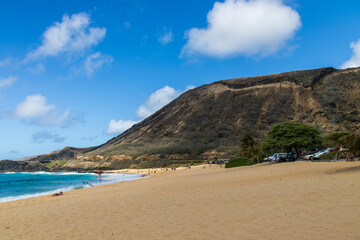Fototapeta na wymiar a beautiful spring landscape at Sandy Beach with blue ocean water, silky brown sand, people relaxing, palm trees and majestic mountain ranges in Honolulu Hawaii USA