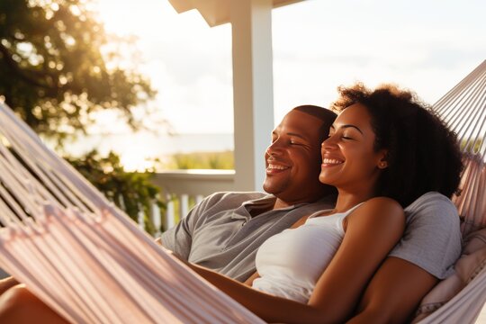 Happy middle-aged afro-american and white couple relaxing and smiling in a hammock on a terrace