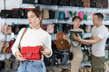 Happy young girl choosing ladies' handbag in clothing shop with large assortment