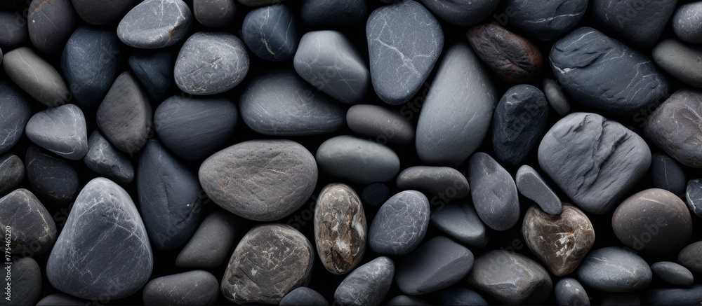 Poster a collection of assorted black and gray rocks stacked closely together on the ground, creating a tex