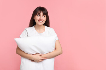 Fototapeta premium Happy woman in pyjama holding pillow on pink background, space for text