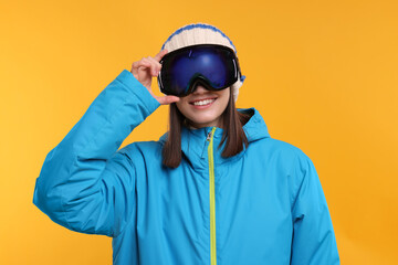 Winter sports. Happy woman with snowboard goggles on orange background