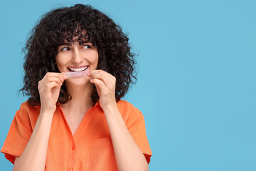 Young woman applying whitening strip on her teeth against light blue background, space for text