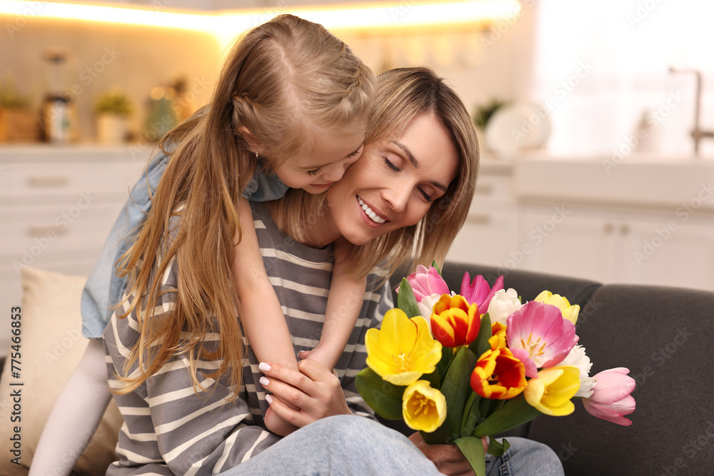 Poster Little daughter congratulating her mom with Mother`s Day at home. Woman holding bouquet of beautiful tulips