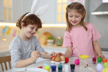 Obraz na płótnie Canvas Easter celebration. Cute children with bunny ears painting eggs at white marble table in kitchen
