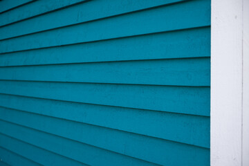 The exterior of a bright blue narrow wooden horizontal clapboard wall of a house. The trim on the...