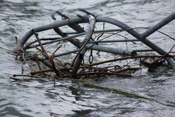 Macro of clutter of metal pipes and branches stuck in a river