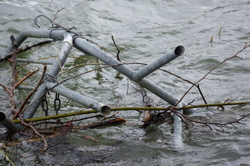 Macro of clutter of metal pipes and branches stuck in a river