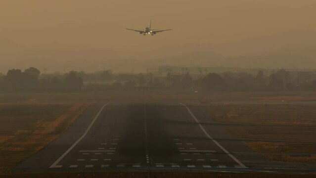 Airplane on final approach to runway during twilight with hazy mountains in the background