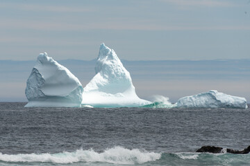 A large white iceberg formation is floating in the cold ocean with layers of textured ice and snow. The ice is in transition melting from the sun's warm rays at sunset. The berg is a blocky shape. - obrazy, fototapety, plakaty