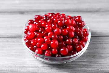 Fresh ripe cranberries in bowl on grey wooden table, closeup