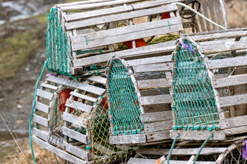 A stack of traditional wooden lobster pots stacked with green mesh nylon rope on the ends of the funnel sections. The baskets have cylindrical shape wood frames. The nets are empty of seafood. - obrazy, fototapety, plakaty