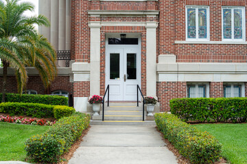 The exterior wall and entrance to a historical brown brick building with tall columns and concrete...