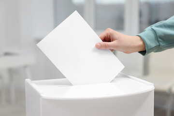 Woman putting her vote into ballot box on blurred background, closeup
