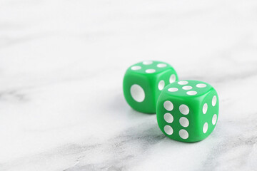 Two green game dices on white marble table, closeup