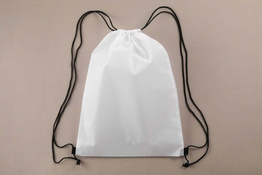 One white drawstring bag on beige background, top view