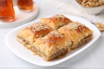 Eastern sweets. Pieces of tasty baklava and tea on white tiled table, closeup