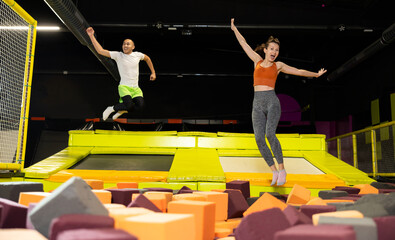 Happy athletes, man and girl, training to jump on trampolines at the trampoline center