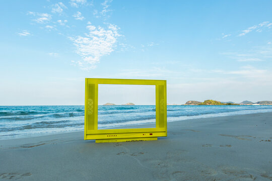 Yellow TV frame on the beach. The blue sky is bright and calm.