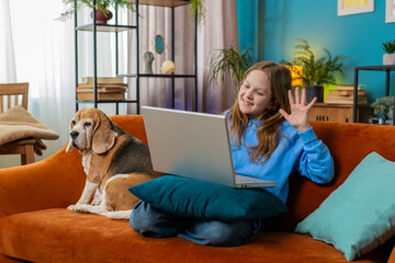 Happy preteen girl making video webcam conference call with friends or family, enjoying pleasant conversation. Smiling child use laptop to talk with teacher, study, education at home sitting on sofa.