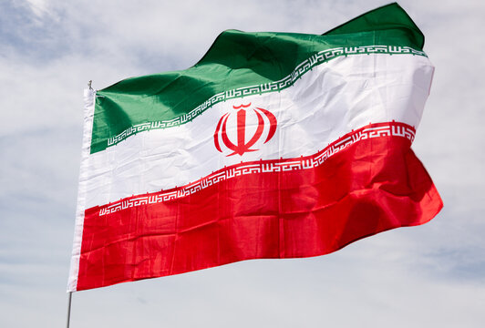 Big flag of Iran fastened on stick against background of blue sky under daylight