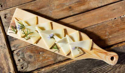 From above of delicious cheese slices served with rosemary sprouts and flowers on wooden cutting...