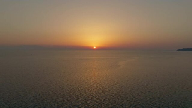The drone retreats, capturing the sunset over the calm sea in warm shades