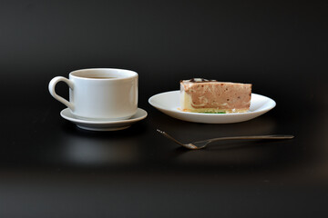 A cup of hot coffee and a plate with a piece of Belgian cream cheesecake on a black background.