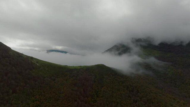 Drone advances through mist revealing the green slopes and valleys of the Basque Country, with the mountain tops shrouded in clouds