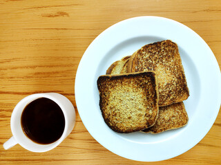 Toasts on white plate and cup of black coffee on wooden background, top view