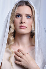 Portrait of a young woman against a background of white fabric. Female head is covered with a white cloth. - 775509821