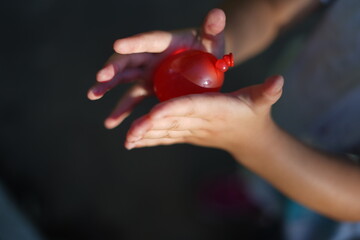 赤い水風船を両手で持つ / Hold a red water balloon with both hands - obrazy, fototapety, plakaty