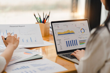 Two businesspeople or an accountant team are analyzing data charts, graphs, and a dashboard on a laptop screen in order to prepare a statistical report and discuss financial data in an office. - obrazy, fototapety, plakaty